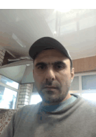 a man wearing a baseball cap and a grey sweater looks at the camera