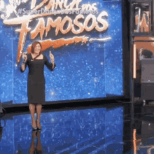 a woman in a black dress stands in front of a sign that says " famosos "