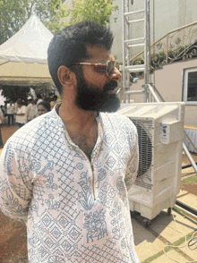 a man with a beard wearing sunglasses stands in front of an air conditioner