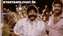 a man with a mustache is standing next to another man in front of a fireworks display .