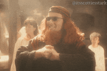 a man with long red hair and a beard wearing sunglasses and a headband with the hashtag @itsscottiesstark