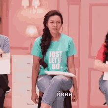 a woman wearing a t-shirt that says just let it go sits on a stool