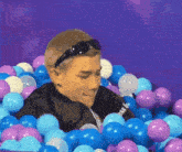 a man wearing sunglasses is sitting in a ball pit filled with blue and purple balloons