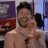 a shirtless man giving a thumbs up in front of a purple gym banner