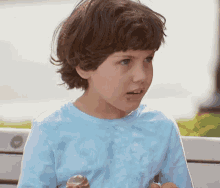 a young boy in a blue shirt is eating an ice cream