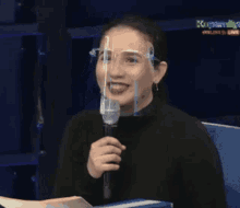 a woman wearing a face shield is laughing and holding a microphone