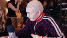 a bald man wearing a gucci jacket is sitting in front of a microphone