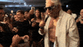 a man without a shirt is singing into a microphone in front of a crowd of people