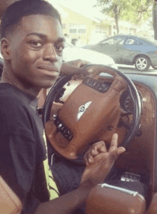 a young man is sitting in a bentley car and giving the middle finger