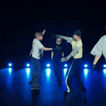 a group of young men are dancing in a dark room with a blue light behind them