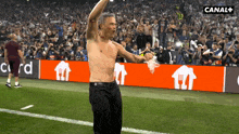 a shirtless man stands on a soccer field in front of a canal + banner