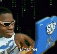 a man wearing sunglasses is looking at a laptop with the words mom rn on the screen