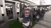 a man in a red bull shirt is standing in front of a building .