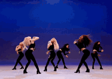 a group of women are dancing on a stage in front of a blue backdrop