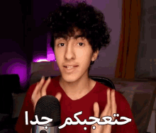 a young man in a red shirt stands in front of a microphone with arabic writing on the bottom