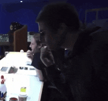 a man talking on a cell phone while another man sits behind him