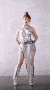 a woman in a silver dress and boots is standing on a tile floor .