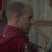 a bald man wearing a red cape looks angry