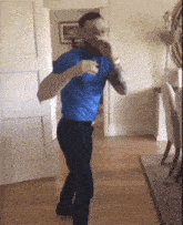 a man in a blue shirt and black pants is dancing in a room