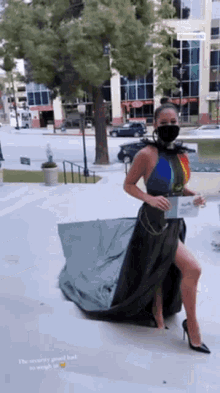 a woman wearing a mask and a long dress is standing on the sidewalk