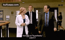 a woman in a lab coat is talking to two men in suits in a hallway .