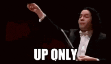 a man in a tuxedo is holding a baton and giving a thumbs up while leading an orchestra .