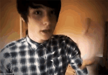 a young man wearing a plaid shirt is making a funny face