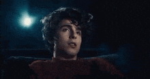 a young man with curly hair is sitting in a chair with his eyes closed in a dark room .