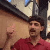 a man with a mustache and a red shirt is giving a thumbs up .