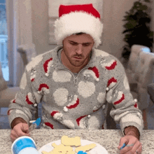a man wearing a santa hat and a sweater decorates cookies