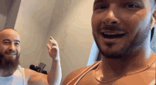a man with a beard wearing a white tank top and a gold chain