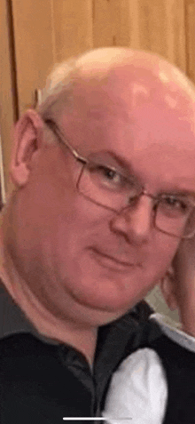 a bald man wearing glasses and a black shirt is smiling .
