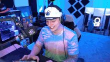 a man wearing a hat and headphones is sitting at a desk playing a video game .