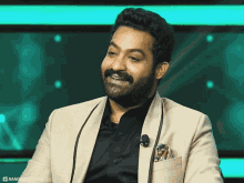 a man with a beard and mustache is wearing a tan jacket and black shirt