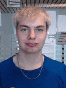 a young man is wearing a blue shirt and a chain around his neck .