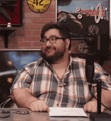 a man in a plaid shirt sits in front of a microphone in front of a sign that says around the corner
