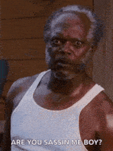 an older man with a beard is wearing a white tank top and talking to someone .