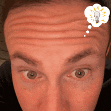 a close up of a man 's face with a light bulb in a thought bubble above his forehead
