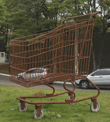 a large shopping cart is sitting in the grass in front of a car