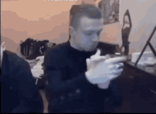 a man in a black sweater is sitting at a table holding a remote control .