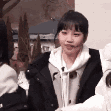a woman wearing a black jacket and a white hoodie is standing next to a group of people .