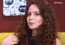 a woman with curly hair is sitting in front of a wall with cats on it and a sign that says love