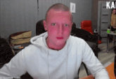 a man in a white hoodie has a red face and the word kai is on the wall behind him