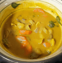 a bowl of yellow soup with carrots and broccoli in it