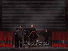 a group of people standing in front of a screen that says kane lives on it
