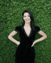 a woman in a black dress is posing for a picture in front of a green hedge .