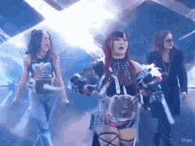 a group of female wrestlers are standing on a stage holding a championship belt .