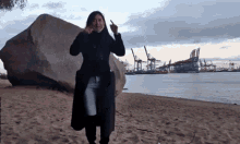 a woman in a black coat is standing on a beach