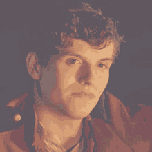 a young man with curly hair wearing a red jacket looks at the camera