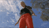 a woman wearing red pants and a black shirt is standing in front of a blue sky .